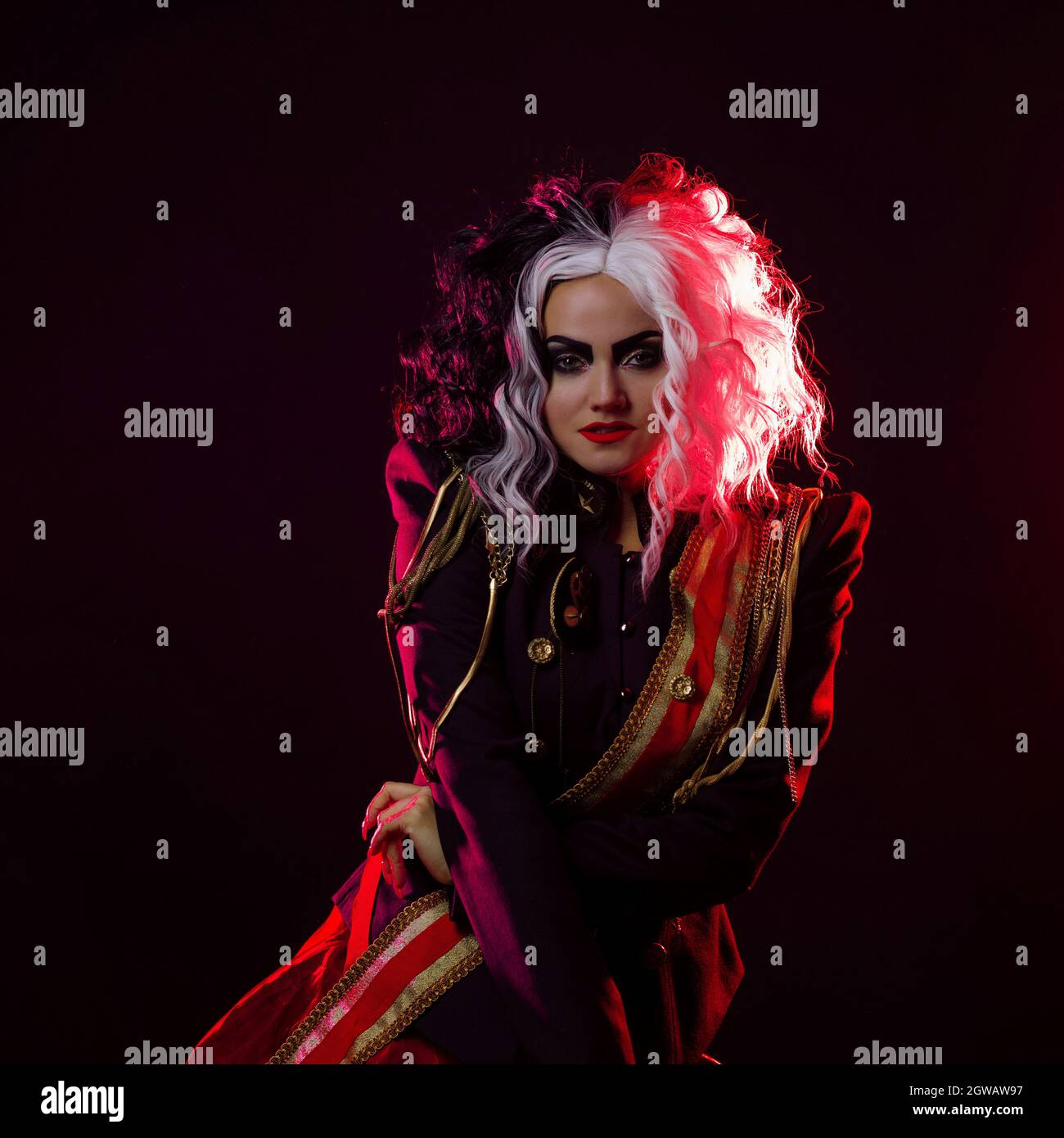 Una donna luminosa e scioccante con un acconciatura in bianco e nero è vestita in una divisa decorata e una gonna piena. Retroilluminazione rossa sul retro. Foto Stock