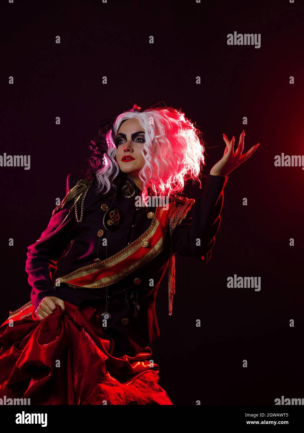 Una donna luminosa e scioccante con un acconciatura in bianco e nero è vestita in una divisa decorata e una gonna piena. Retroilluminazione rossa sul retro. Foto Stock