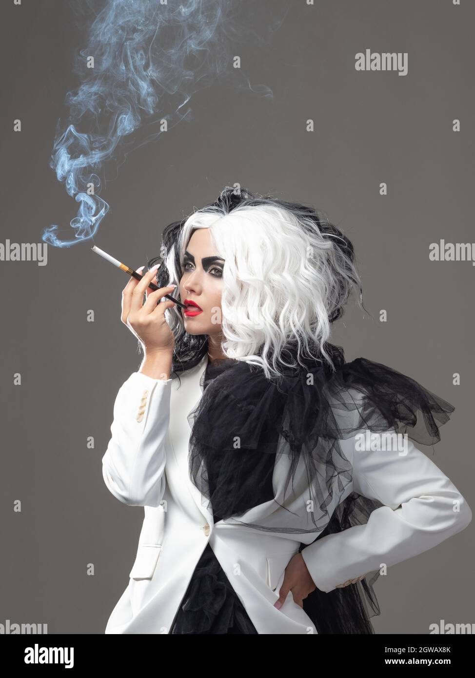 Una donna carismatica insolita in un abito bianco e nero con capelli bianchi e neri fuma una sigaretta utilizzando un boccaglio, un'immagine audace ed elegante di un Foto Stock