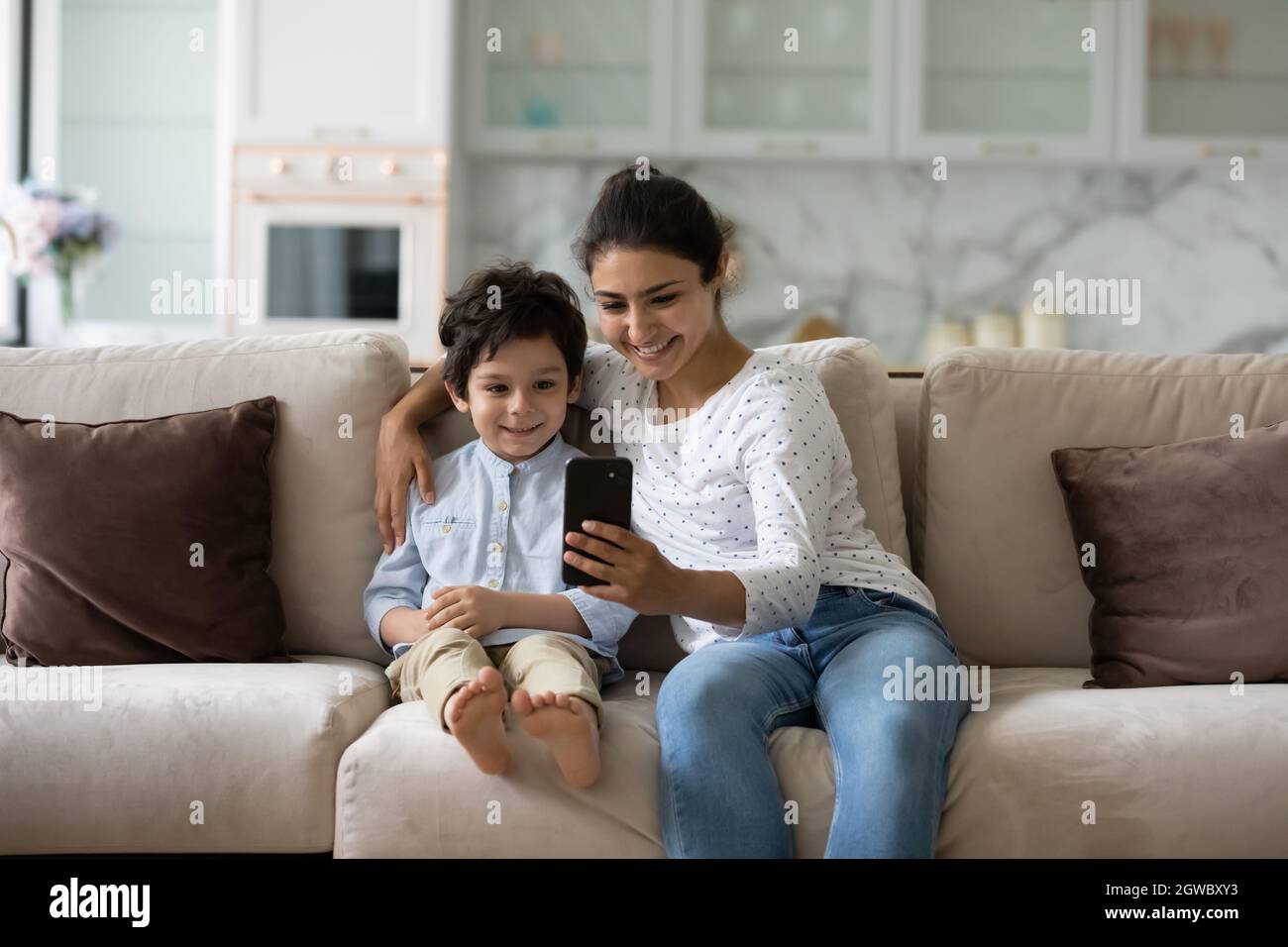 Sorridendo che lega la giovane donna indiana usando il cellulare con il bambino piccolo. Foto Stock