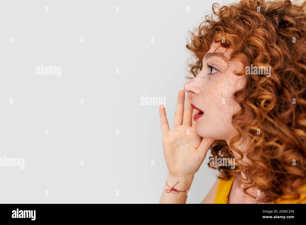 Giovane donna capelli rossi ha messo la sua mano a faccia e grida a qualcuno isolato su sfondo bianco. . Foto di alta qualità Foto Stock