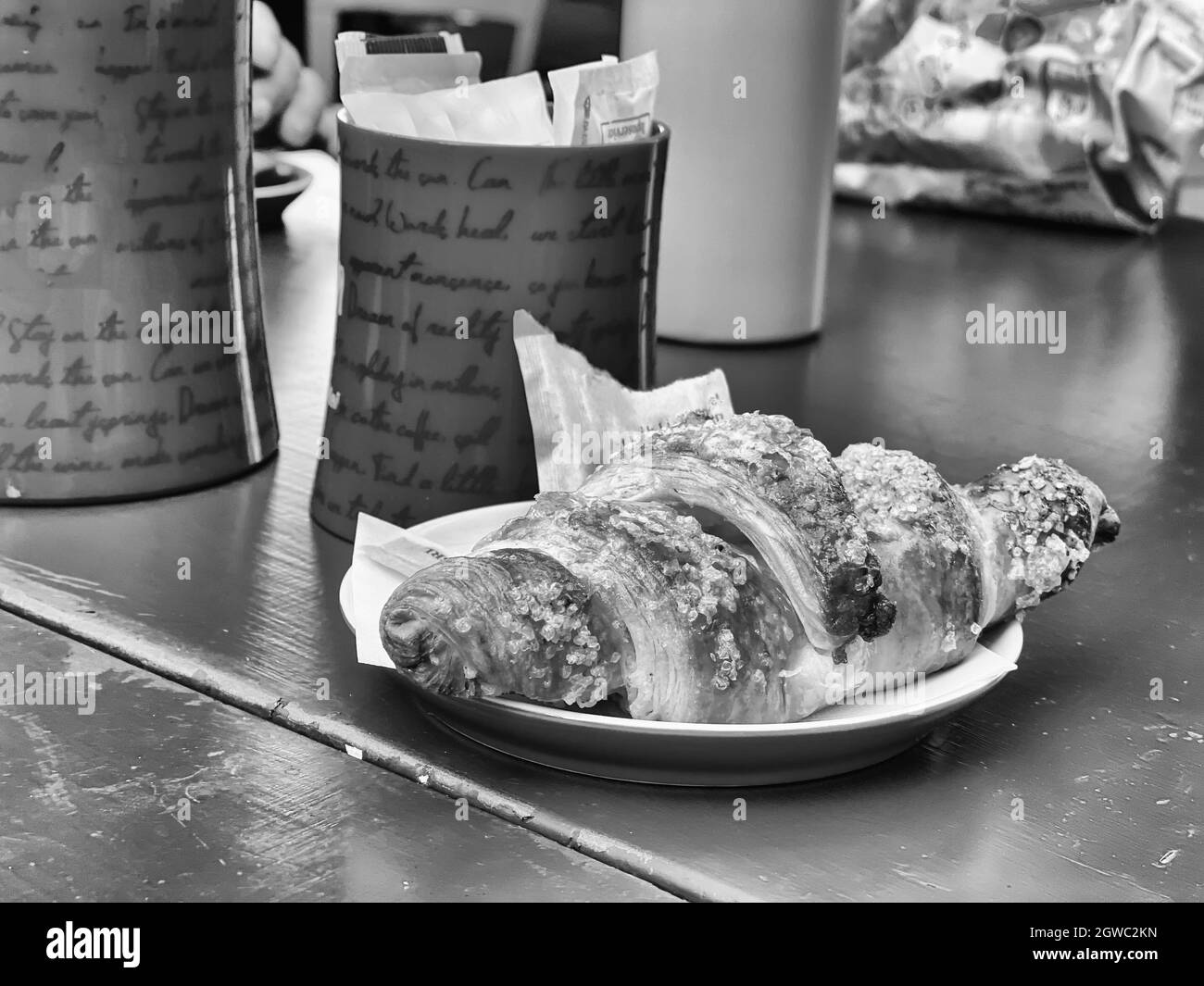 Una foto in scala di grigi di deliziosi croissant appena sfornati su un piatto di ceramica su un tavolo in un caffè Foto Stock
