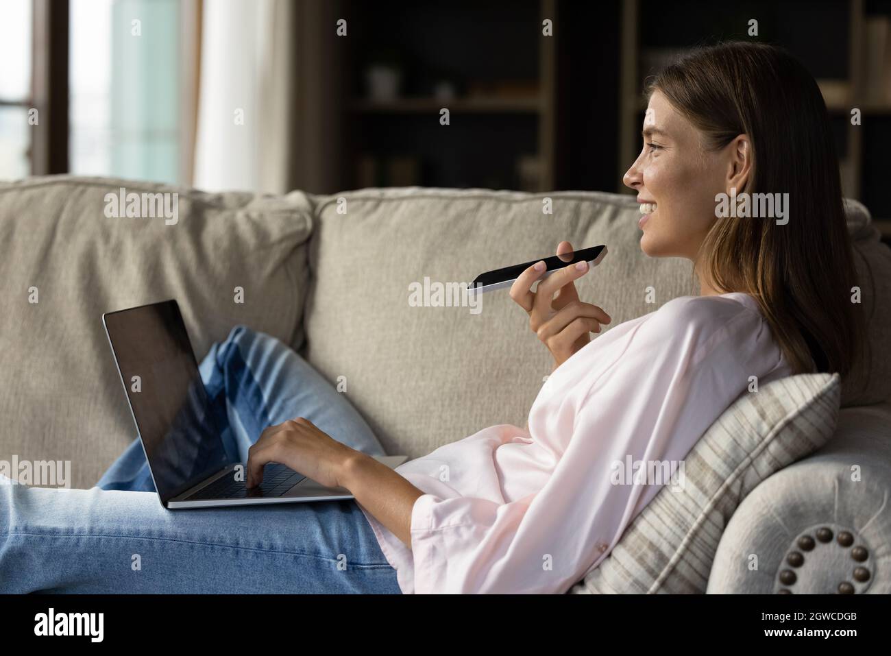 Felice giovane donna che riposa su un morbido e accogliente divano con gadget Foto Stock