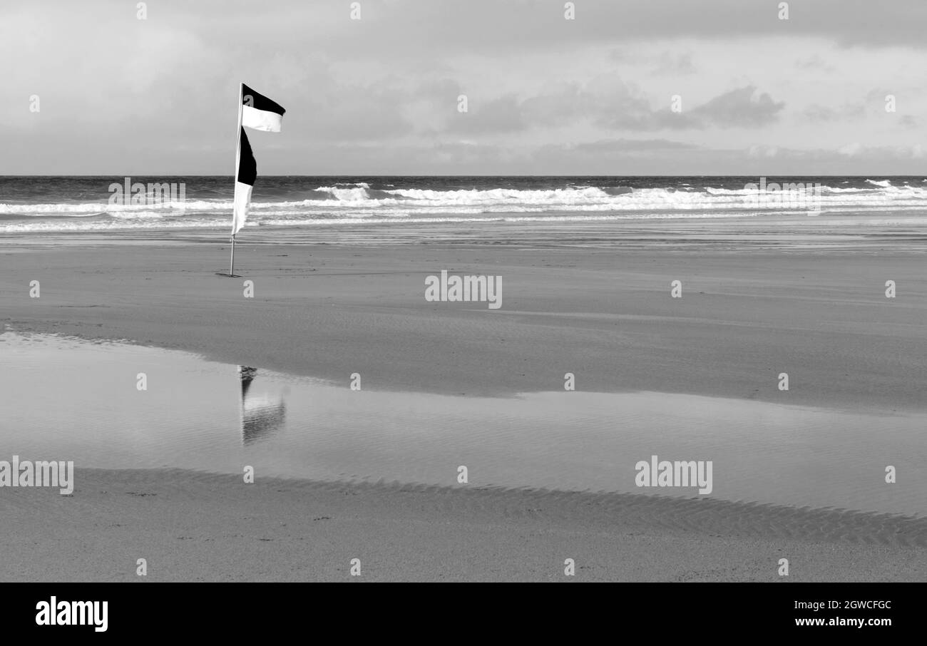 Bandiere RNLI su una spiaggia che denotano l'area sicura per nuotare o fare surf. I riflessi sono visibili nell'acqua di primo piano Foto Stock