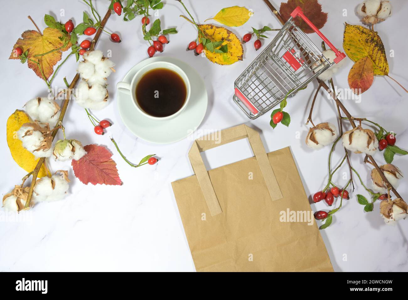 carta da spesa, sacchetto di carta e una tazza di caffè su sfondo di marmo chiaro con decorazione naturale delle foglie autunnali, concetto di vendita stagionale per le vacanze, spazio copia, Foto Stock