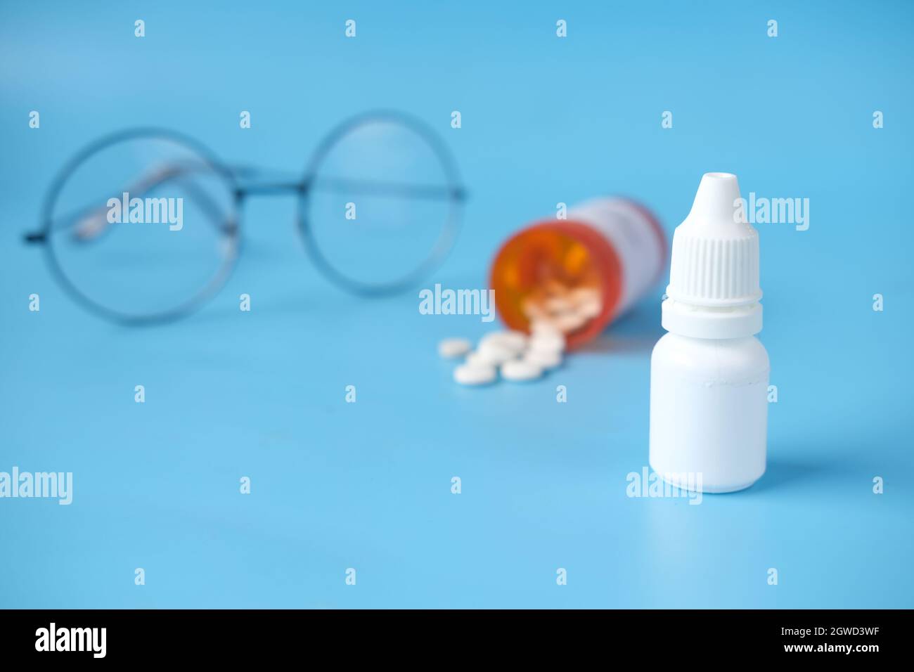 primo piano della bottiglia di goccia dell'occhio e dell'occhiale su sfondo blu , Foto Stock