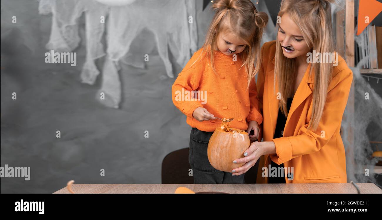 Halloween ritratto di mamma e figlia ragazza toglie i semi di zucca con un cucchiaio per preparare un jack-o-lanterna per l'autunno Holiday.Place per il testo Foto Stock