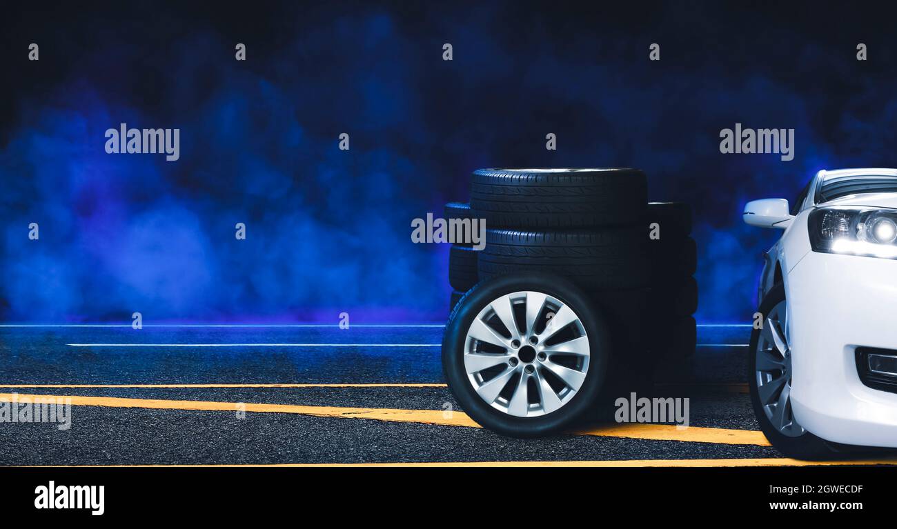 Ruote e pneumatici impilati su strada asfaltata e fumo blu con sfondo nero di notte, Automotive Parts Concept. Foto Stock