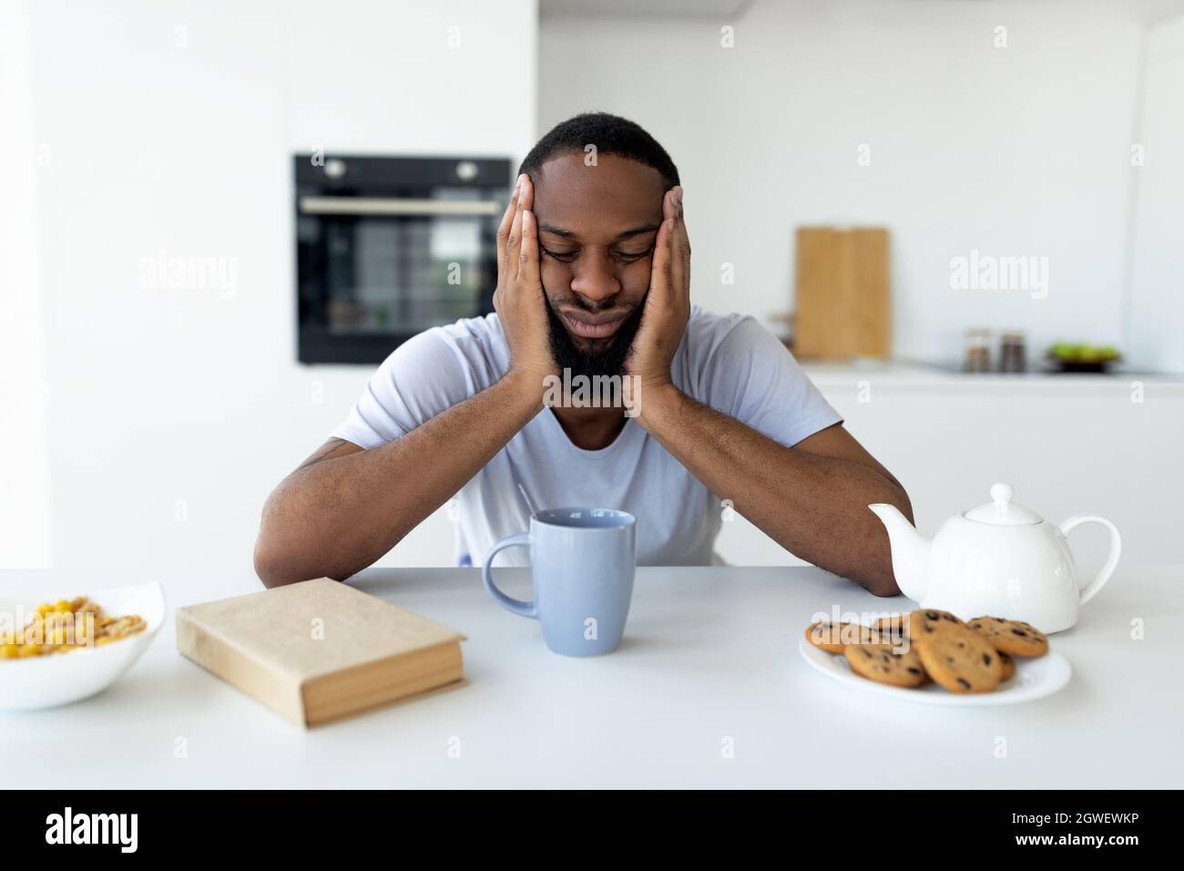 Mancanza di concetto di sonno. Esausto giovane africano americano uomo che soffre di insonnia o stress, seduto e dormire a tavola da pranzo in cucina, selezionare Foto Stock