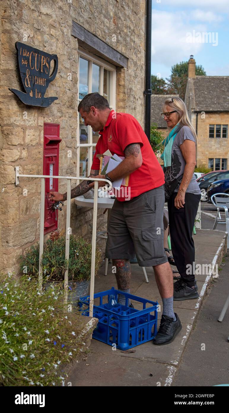 Guiting Power, Gloucestershire, Inghilterra, Regno Unito. 2021. Addetto postale nella sua camicia rossa uniforme che blocca una cassetta delle lettere dopo aver tolto le lettere nella campagna Foto Stock