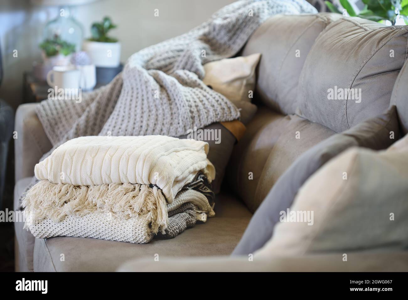 Pila di una varietà di coperte di tiro a maglia morbida impilata su un divano in un soggiorno stile fattoria. Messa a fuoco selettiva primo piano e sfondo sfocati. Foto Stock