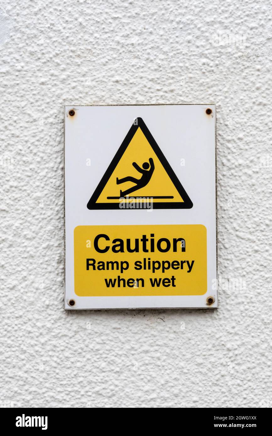 Un segnale di avvertenza indica che la rampa di attenzione è scivolosa quando è bagnata. Foto Stock