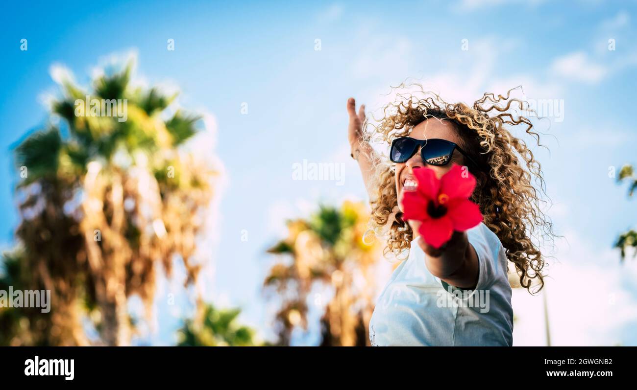 Felice bella donna in occhiali da sole con capelli ricci sensazione eccitato tenendo rosso fiore con le braccia tese contro il cielo. Donna allegra che ha f Foto Stock