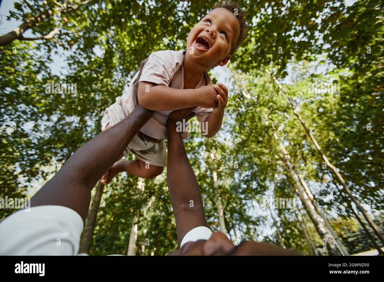 Vista ad angolo basso a bambino carino ridendo felicemente mentre gioca con il padre nel parco contro gli alberi, spazio di copia Foto Stock