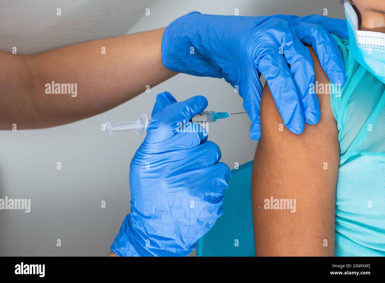 l'infermiere dei bambini che inietta il braccio della bambina marrone, la ragazza che guarda l'iniezione. le mani del medico con i guanti di gomma che inietta il covid-19 o il vaccino influenzale. med Foto Stock