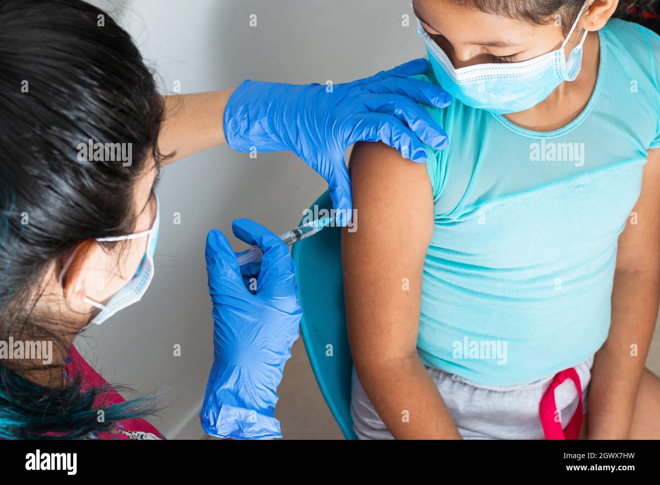 l'infermiera dei bambini che inietta il braccio della ragazza marrone. la mano del medico con i guanti di gomma che inietta il vaccino di covid-19. il vaccino di flu. il concetto medico, la salute e la padella Foto Stock