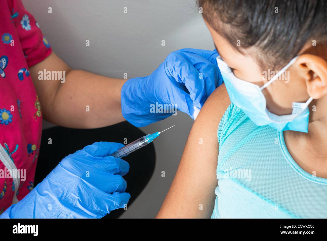 l'infermiera dei bambini pulendo il sangue con la lana di cotone dopo la somministrazione dell'iniezione nel braccio della ragazza marrone. il medico iniettando il vaccino contro covid-19. influenza vacci Foto Stock