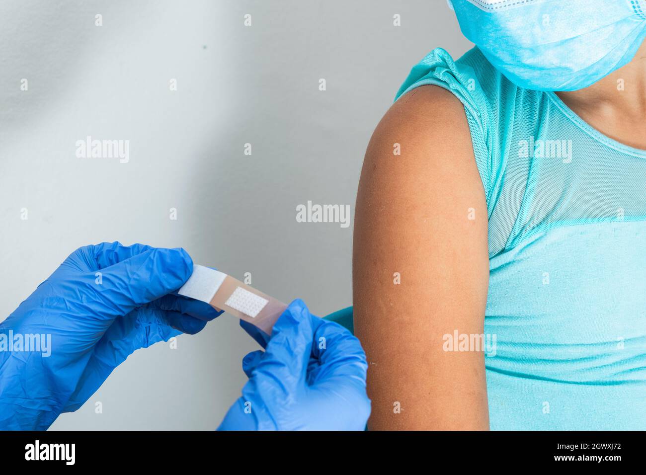 Medico in guanti protettivi di gomma blu mettendo un bendaggio adesivo sul braccio di una ragazza dopo aver ferito la pelle o iniettato il vaccino. Pronto soccorso. Medico, p Foto Stock