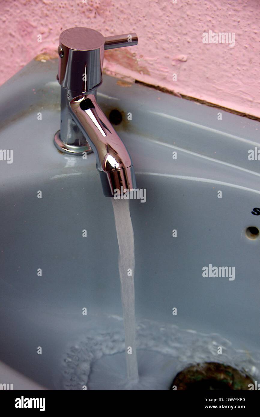 Vista del lavabo di colore grigio in cui l'acqua scorre attraverso il rubinetto aperto Foto Stock