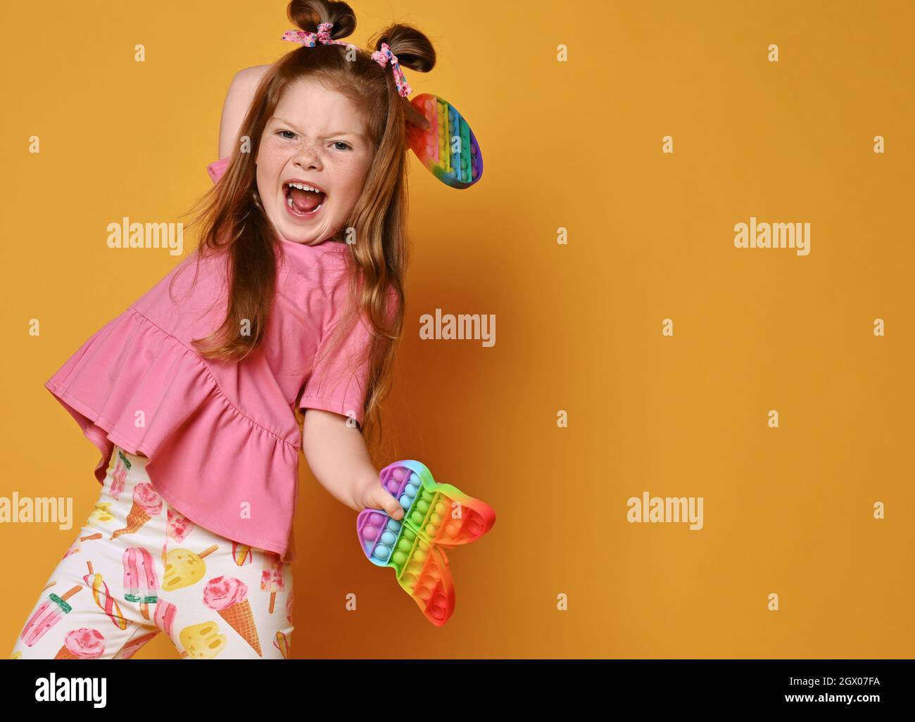 Ragazza che urla in abiti colorati danze tenendo due sensoriali arcobaleno colore giocattoli rotondo e farfalla pop in mani Foto Stock