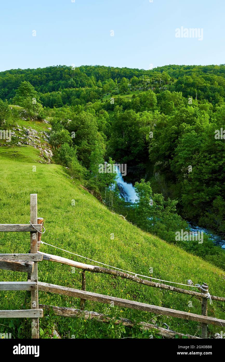 Paesaggio montano con cascata e sentiero in legno. Vegetazione estiva e piante in montagna Foto Stock