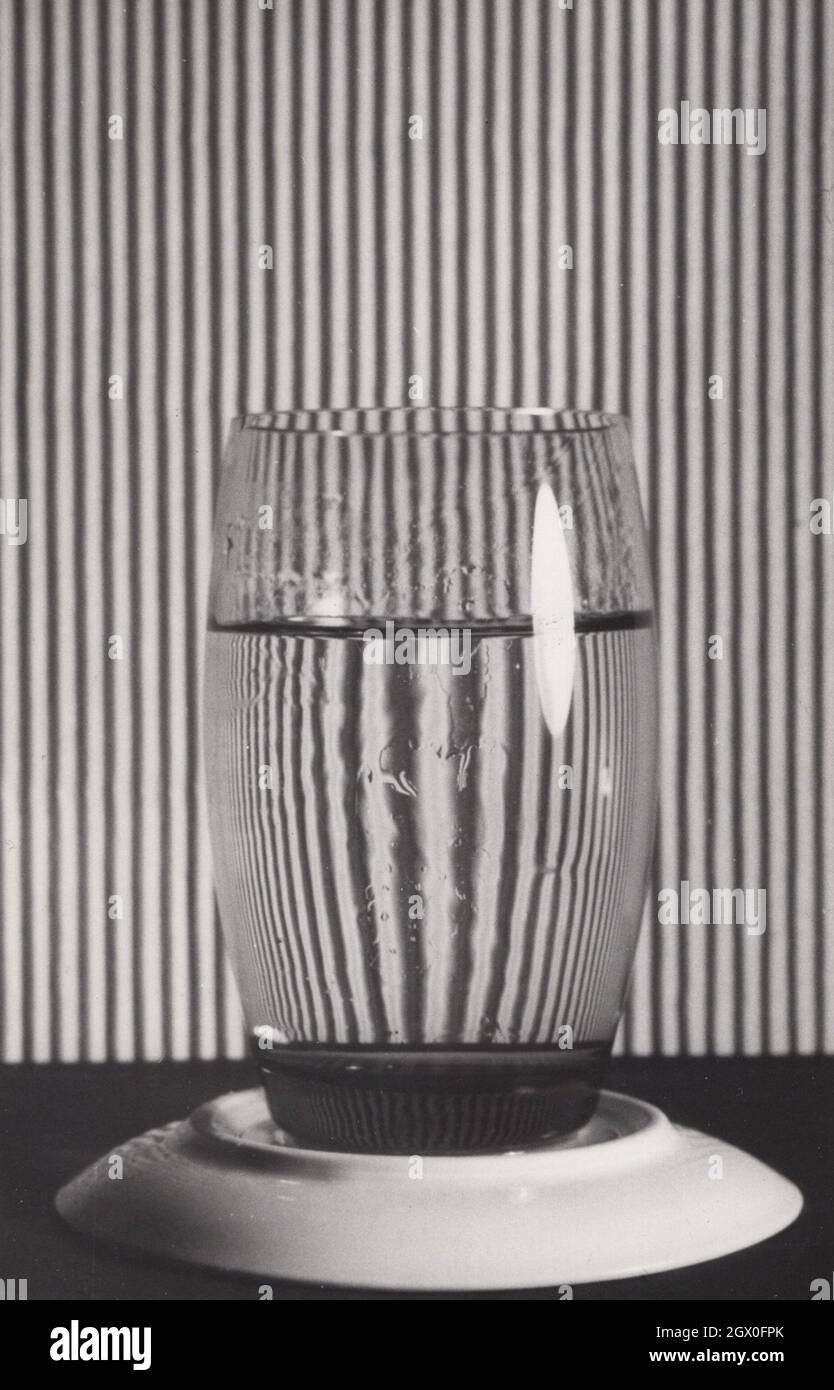 foto d'arte d'epoca super rara degli anni '60 o '70. Questa foto monocromatica mostra un vetro quasi pieno di acqua. Vedere attraverso il vetro la schiena è un po' iridescente e più grande di quanto non sia realmente. Si tratta di una foto artista molto creativa e unica. Fonte: Fotografia originale Foto Stock