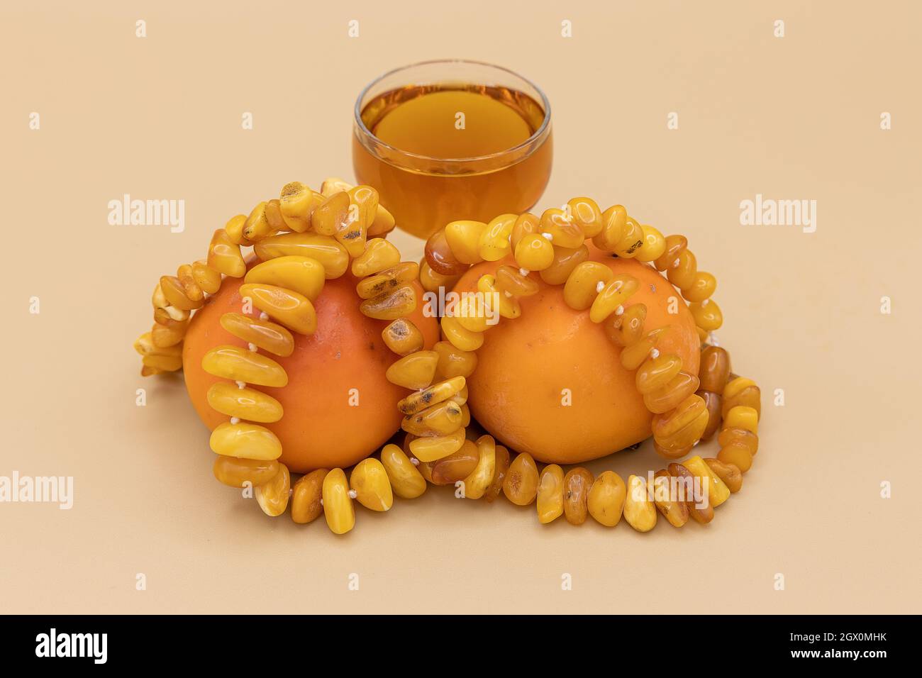 Belle perline ambrate, due persimmoni, e un piccolo bicchiere di rum su sfondo naturale. Composizione Golden Fall Foto Stock