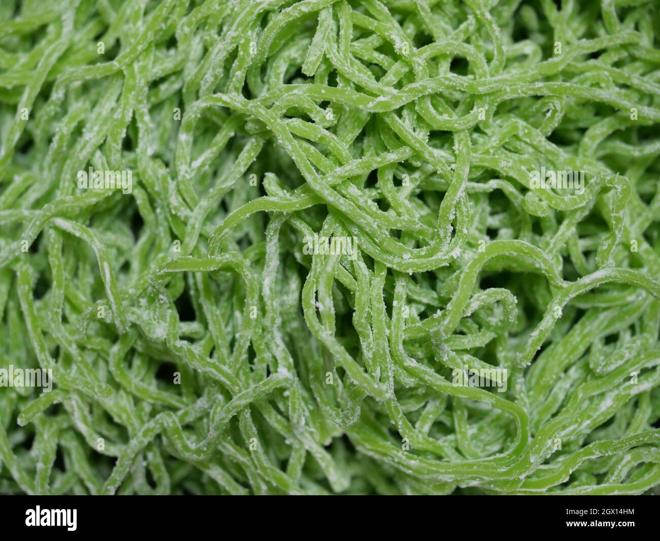 Fuoco selettivo di spaghetti crudi di uova di giada verde, sfondo di modello da spaghetti cinesi e farina Foto Stock