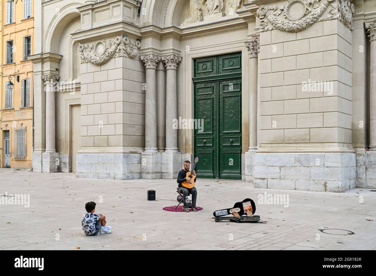 Un ragazzo giovane che ascolta un musicista di strada di fronte all'Église de la Madeleine ad Aix-en-Provence, nel sud della Francia Foto Stock