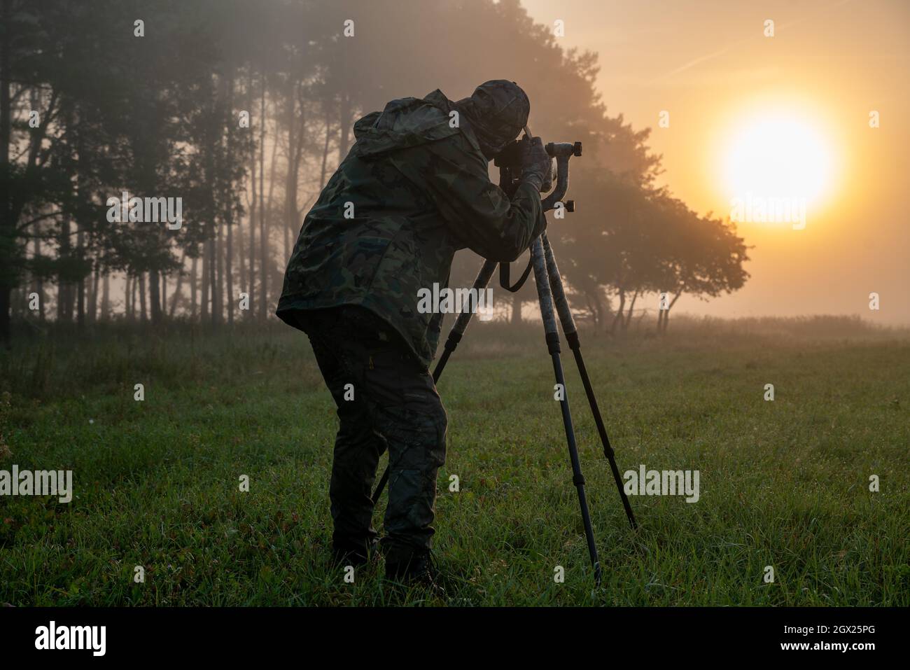 Fotografo della natura in piedi in abiti camuffati con una macchina fotografica su un cavalletto Foto Stock