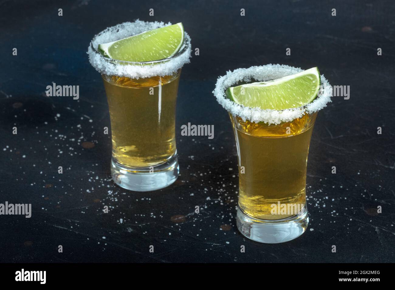 Due colpi di tequila d'oro, con bordi di sale e fette di lime, su sfondo nero Foto Stock
