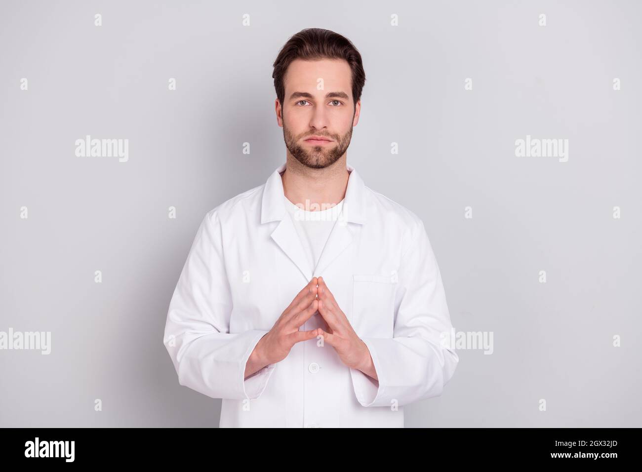 Foto di serio sicuro giovane doc uomo vestito bianco cappotto sorridente braccia insieme isolato grigio sfondo di colore Foto Stock
