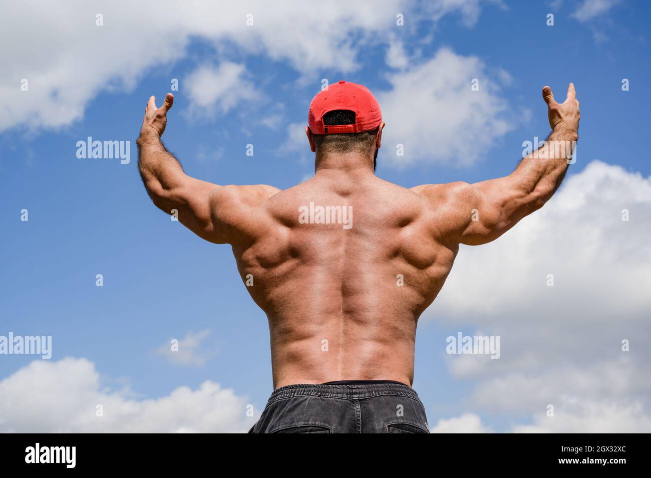 forte giovane maschio in testa rossa alzando le mani verso cieli blu mostrando forti e potenti muscoli posteriori Foto Stock