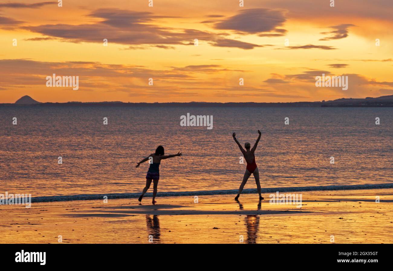 Portobello, Edimburgo, Scozia, tempo britannico. 4 ottobre 2021. Nuvoloso sorgere del sole al mare per Makiko ed Emily mentre si esercitano sulla riva prima di andare per un tuffo freddo nel Firth of Forth. Nella foto: Due amici Makiko ed Emily sono in missione per nuotare in acqua fredda all'alba tutti i giorni nel mese di ottobre. Credit:Arch White/Alamy Live News. Foto Stock