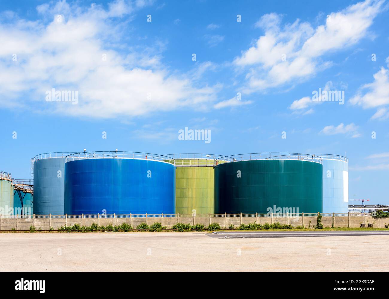 Grandi serbatoi colorati di stoccaggio per olio e carburante in una fattoria di serbatoi sotto un cielo blu con nuvole bianche. Foto Stock