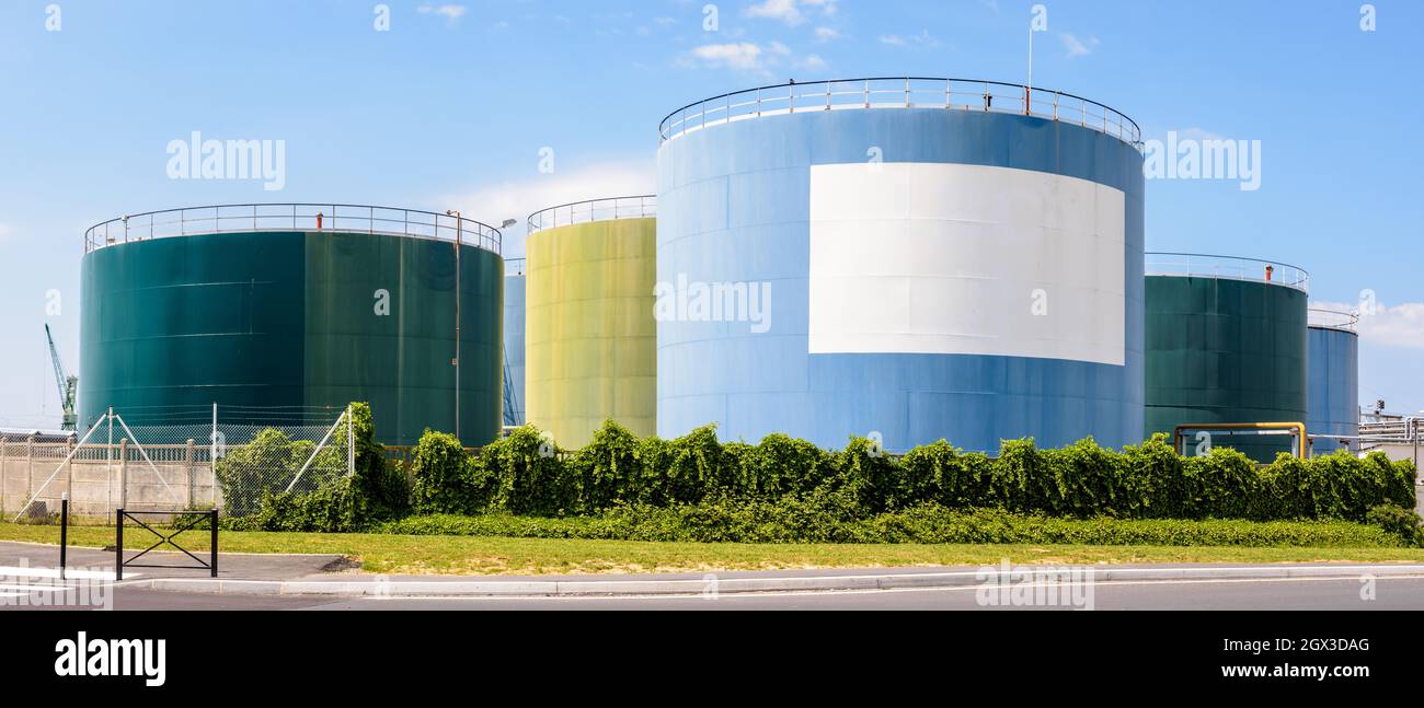 Vista panoramica di grandi serbatoi colorati per l'olio e il carburante in un terminale dell'olio con uno spazio vuoto bianco per la copia sotto un cielo blu. Foto Stock