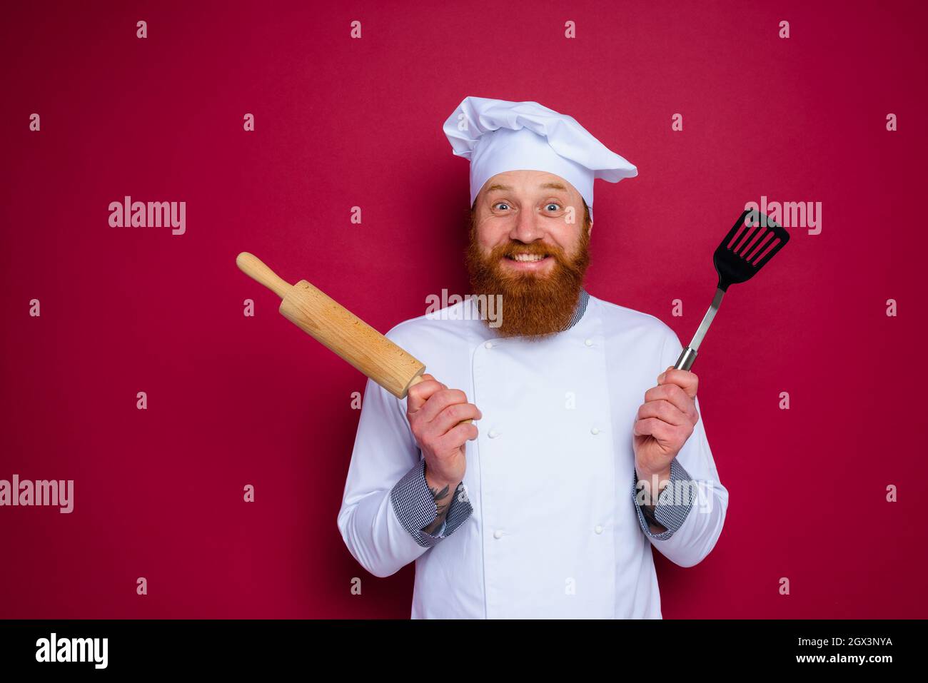 lo chef felice con barba e grembiule rosso tiene la spina di legno Foto Stock