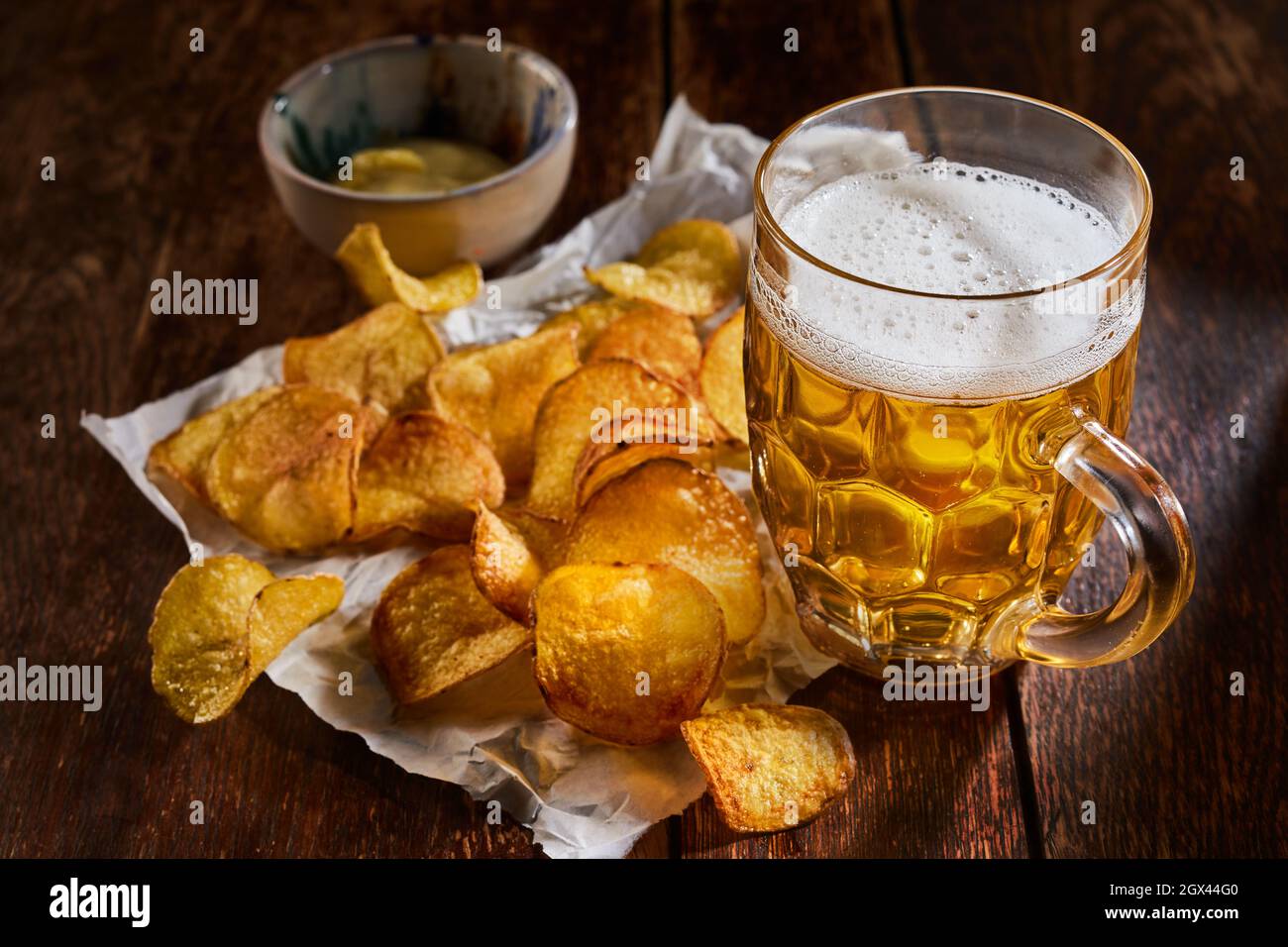 Alto angolo di bicchiere di birra fredda posto con mucchio di patatine croccanti sul tavolo di legno al bar Foto Stock
