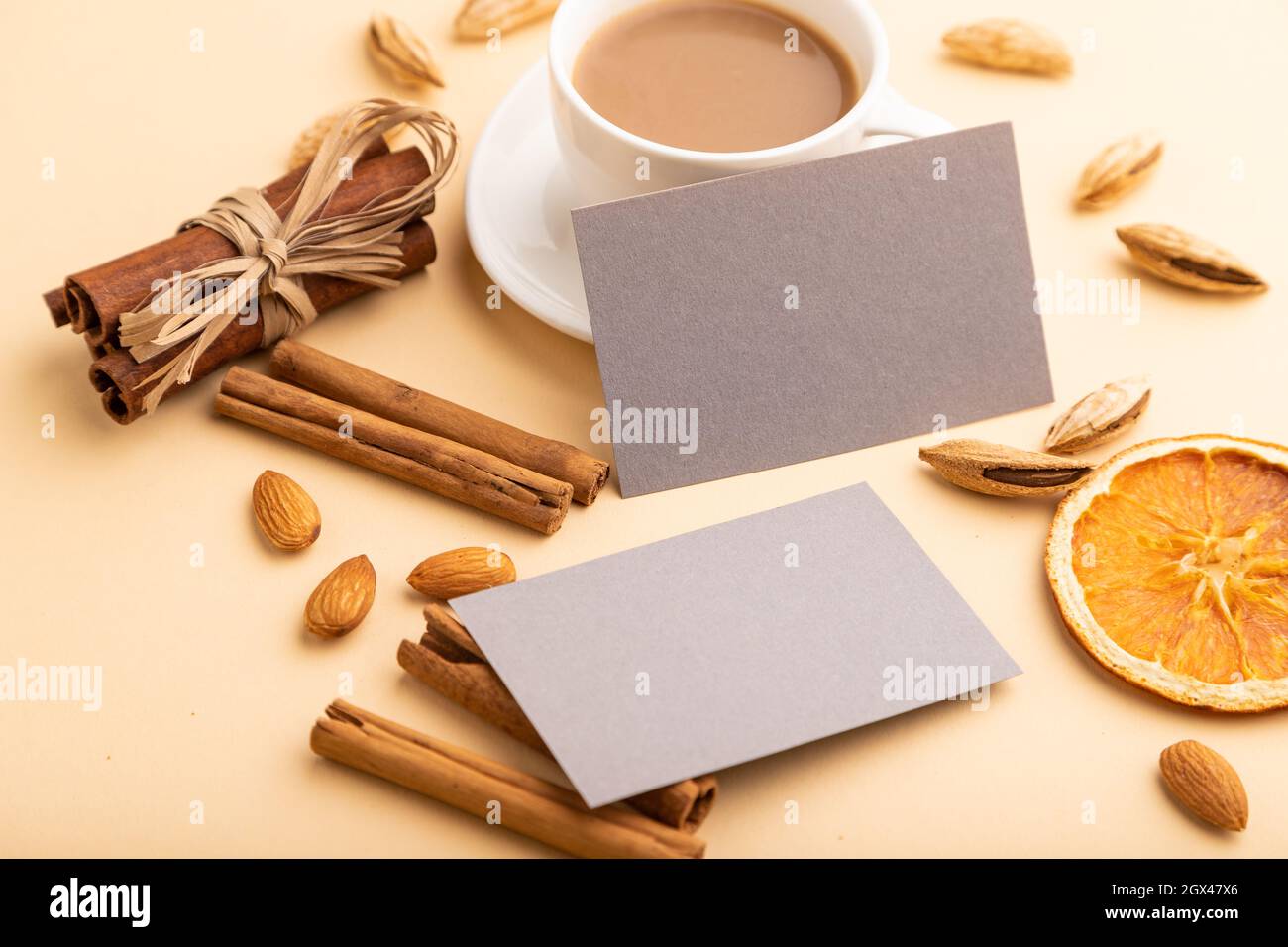 Composizione di biglietti da visita di carta grigia, mandorle, cannella e tazza di caffè. Mockup su sfondo arancione. Vuoto, vista laterale, fermo immagine, spazio per la copia. Foto Stock