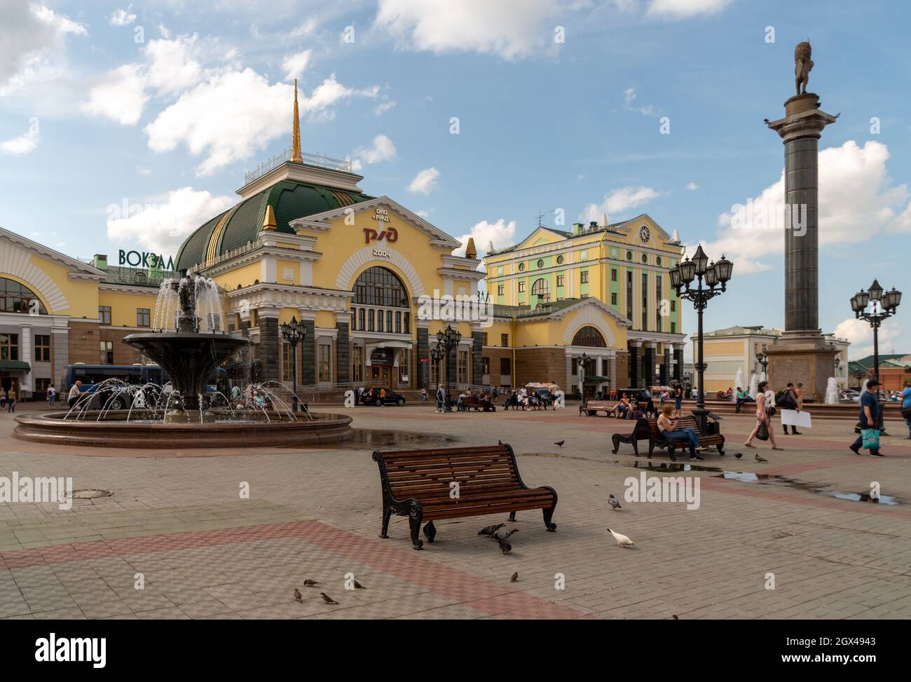 I piccioni camminano vicino ad una panchina in Piazza Privokzalnaya di fronte alla stazione ferroviaria principale con il logo delle Ferrovie russe in russo sulla facciata. Foto Stock