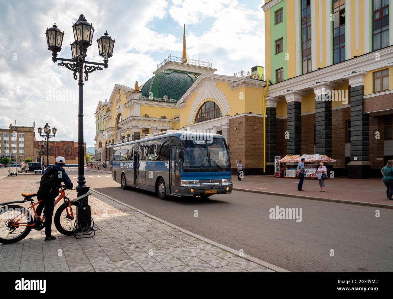 Un ciclista vicino ad un lampione guarda ad un autobus che passa accanto alla stazione ferroviaria principale della città. Foto Stock