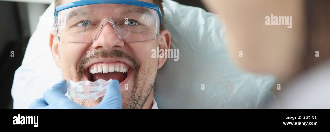 Dottore cerca di proteggere il bocca di plastica per un giovane uomo sorridente per correggere il morso Foto Stock