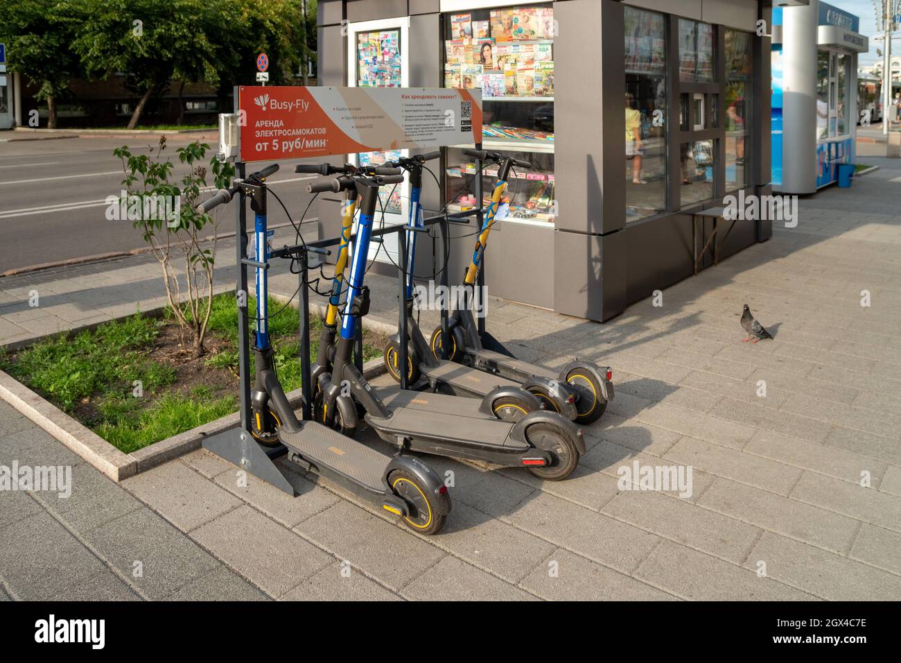 Il parcheggio di scooter elettrici accanto al chiosco per la vendita di un giornale di riviste con le regole di noleggio attraverso l'applicazione a Russi Foto Stock