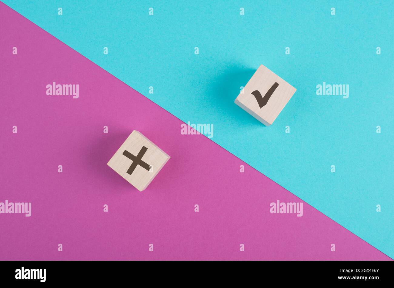 Cubi di legno con segno di spunta e croce su uno sfondo rosa e blu vibrante, minimalismo Foto Stock