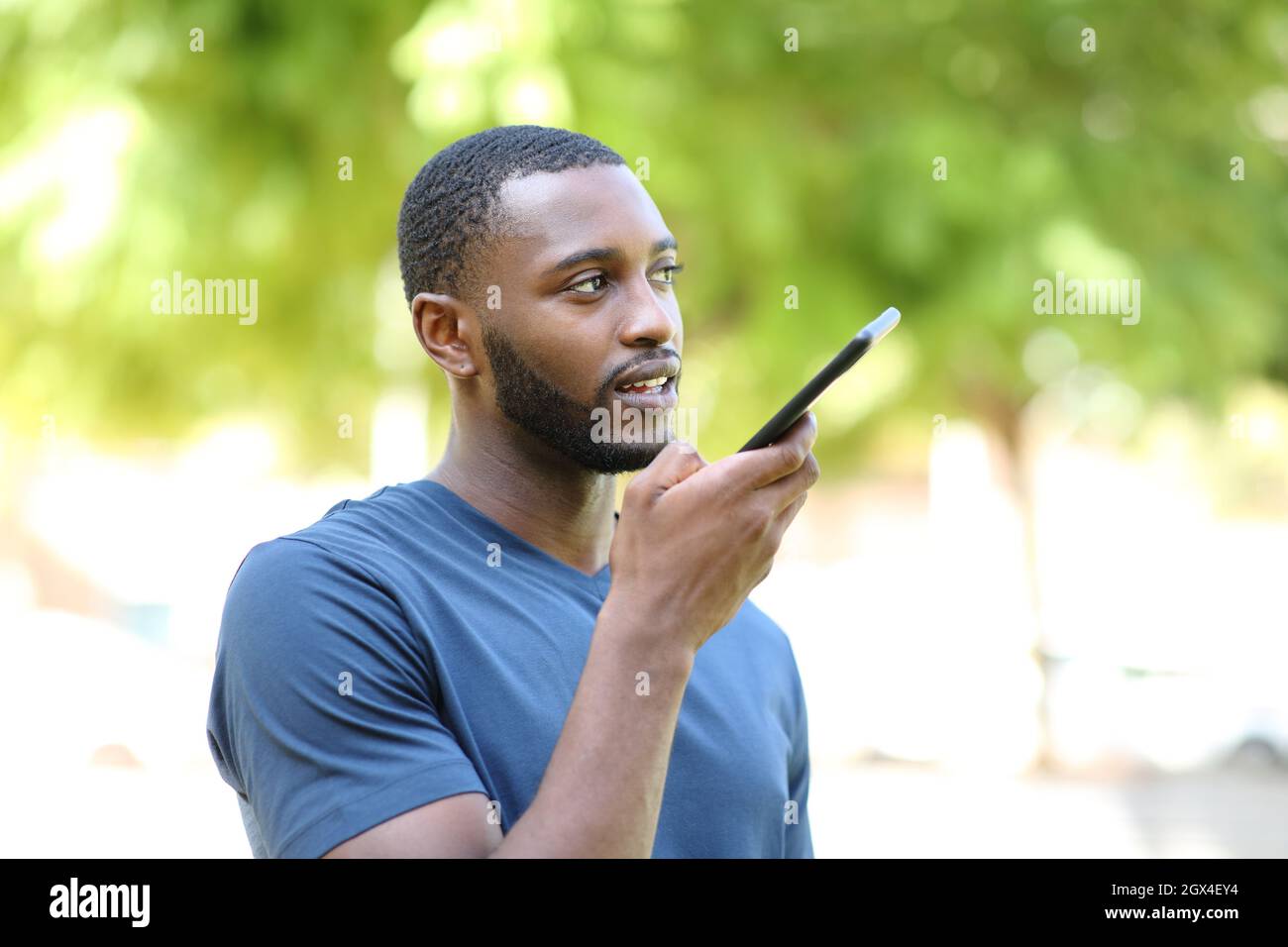 Uomo nero che detta il messaggio audio sullo smartphone che cammina in un parco Foto Stock