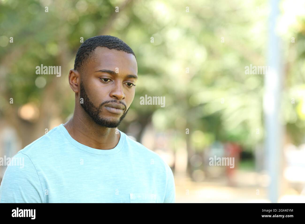 Triste uomo nero che guarda via distratto a camminare in un parco Foto Stock