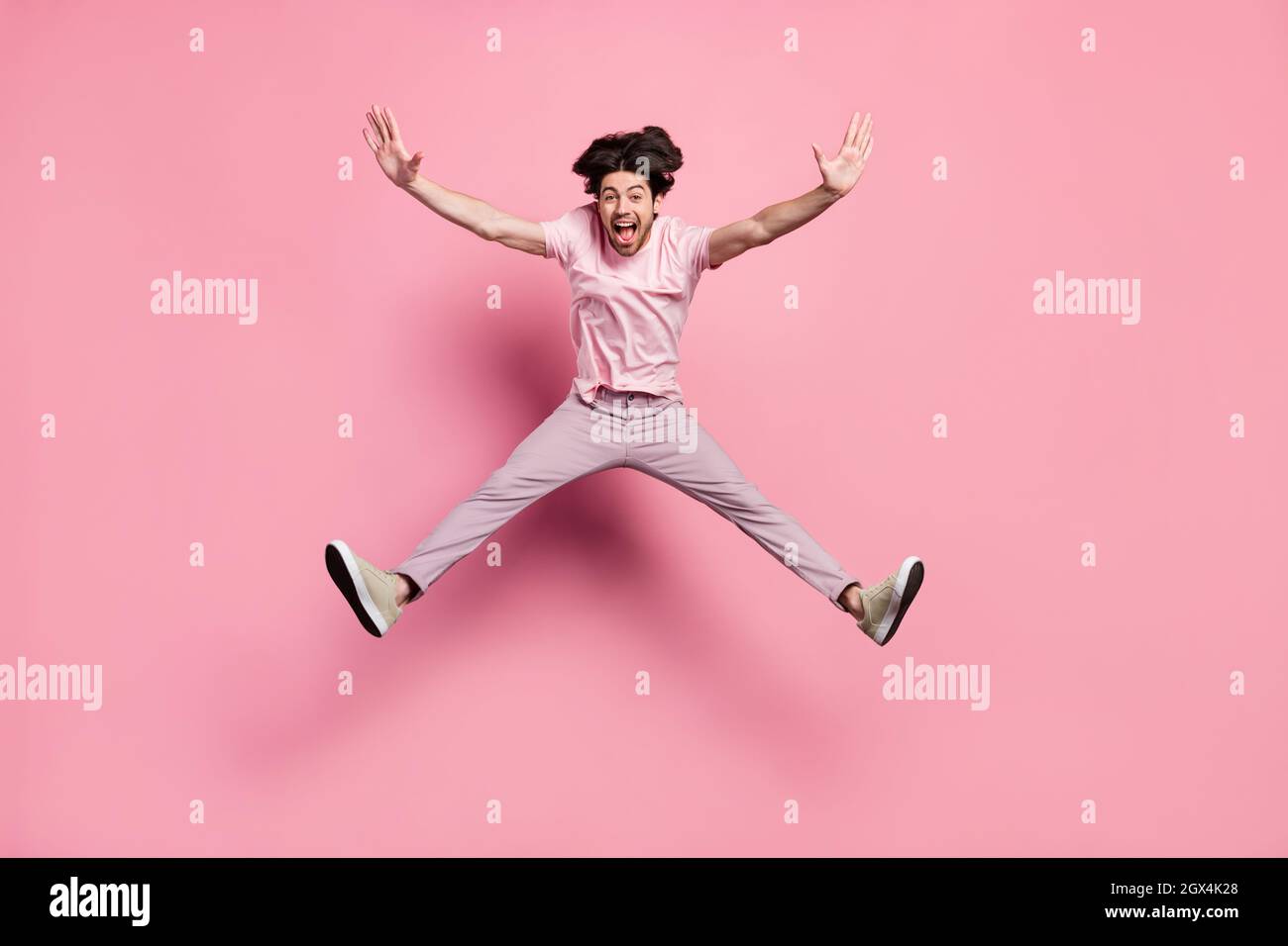 Uomo di dimensioni complete che indossa abiti casual volando su forte vento isolato colore rosa pastello sfondo Foto Stock