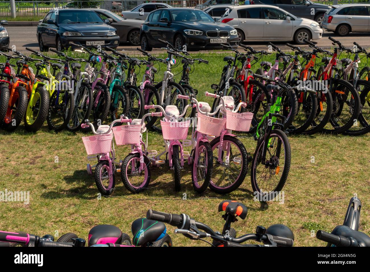 Le biciclette rosa per bambini sono in vendita e noleggiate sul prato di fronte alle auto in una giornata estiva. Foto Stock