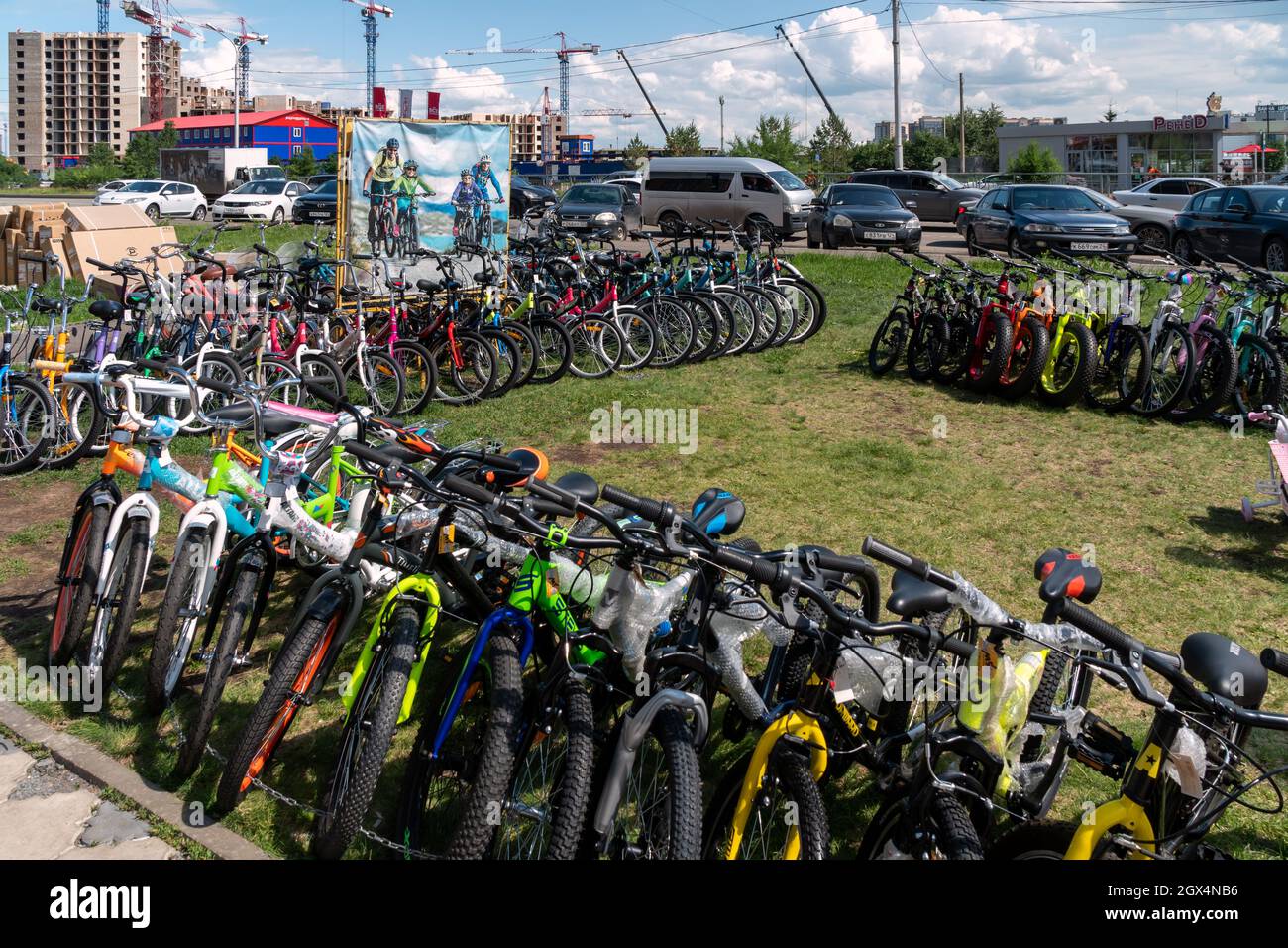 Diverse biciclette sono esposte in vendita e noleggiate sul prato sullo sfondo di un cantiere vicino a una strada cittadina in una giornata estiva. Foto Stock