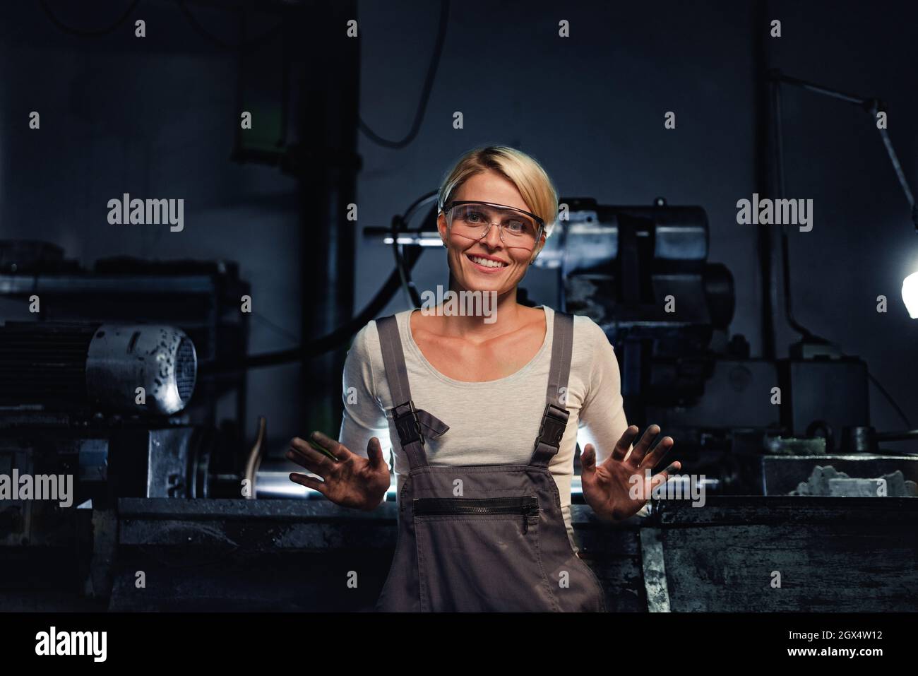 Ritratto di felice giovane donna industriale con le mani sporche guardando la macchina fotografica in interni in metallo officina. Foto Stock